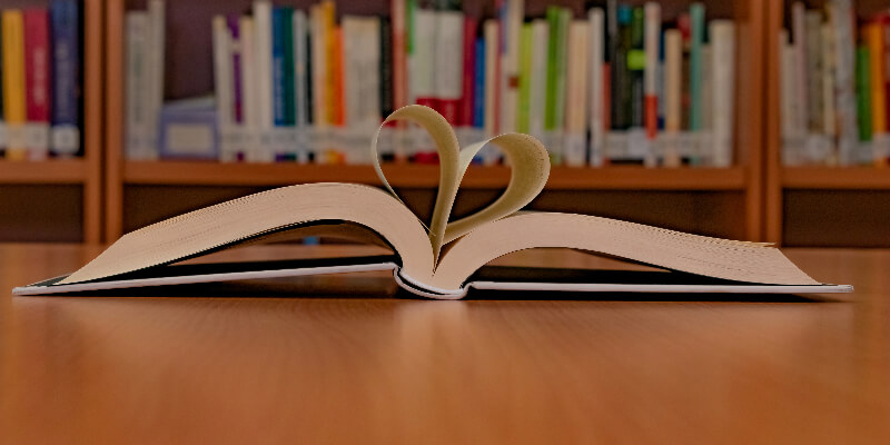 a backdrop of a books on shelves and a pickture of a book opened with some of the pages forming a heart.