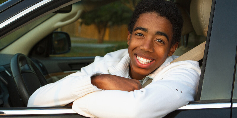 A teen sitting in the driver's seat with their sitbelt on, smiling at the camera.